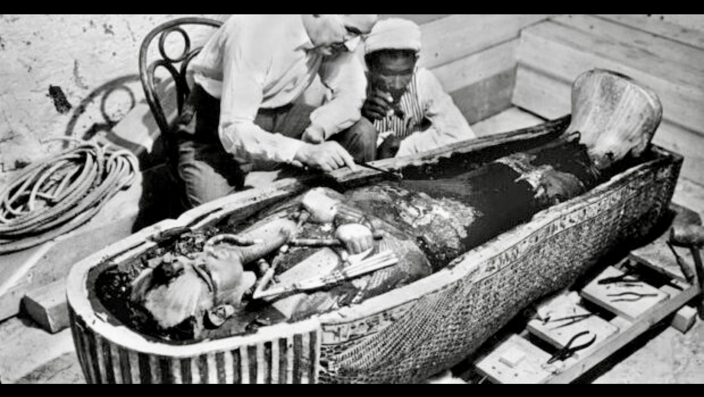Howard Carter examining artefacts inside the tomb of Pharaoh Tutankhamun shortly after the burial chamber was opened in February 1923. (Public domain archival photograph)