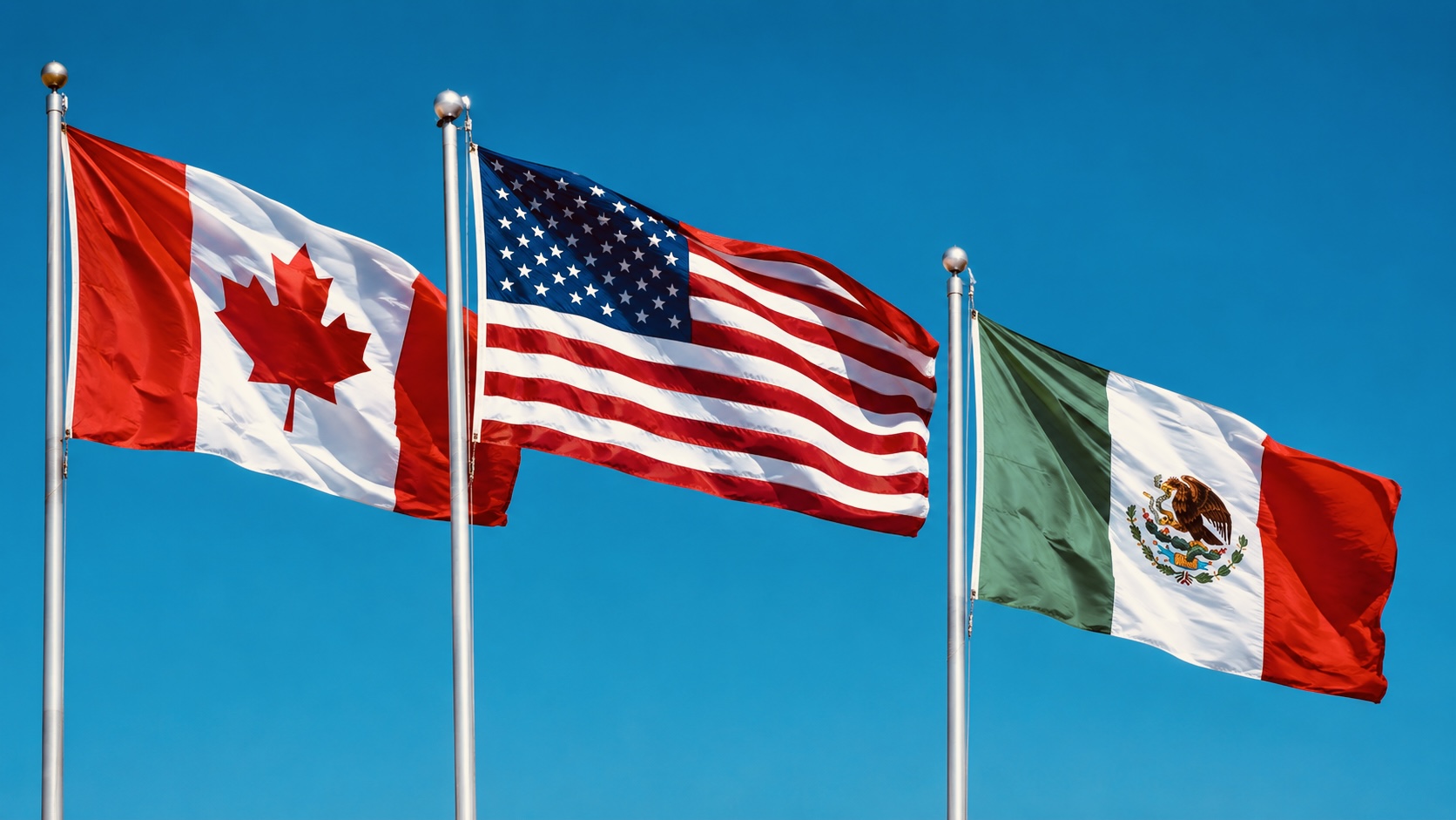 The national flags of Canada, the United States, and Mexico fly side by side against a clear blue sky, representing the North American trade partnership.