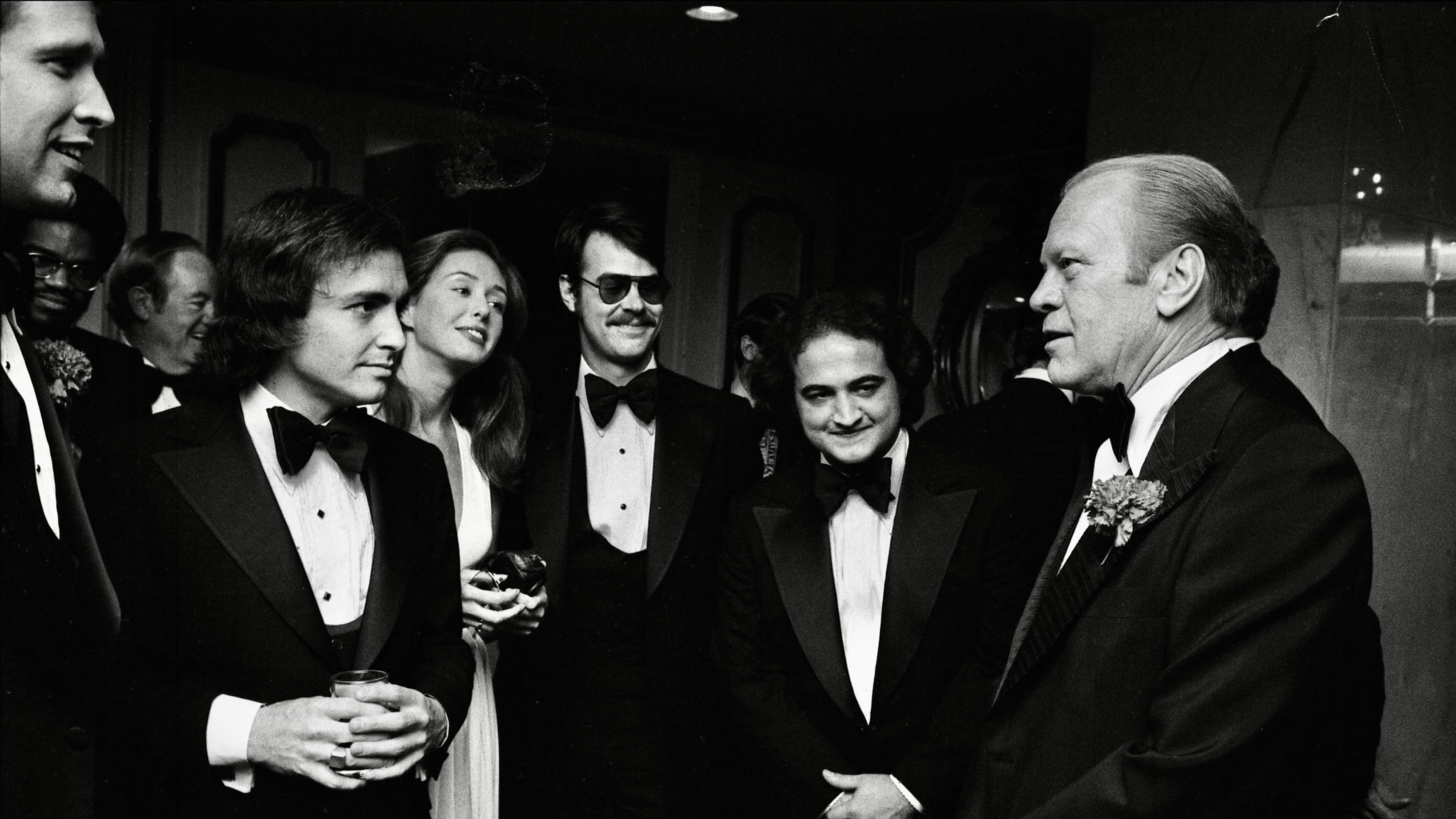 Saturday Night Live creator Lorne Michaels and cast members Dan Aykroyd and John Belushi speaking with President Gerald Ford at a Washington dinner in March 1976.