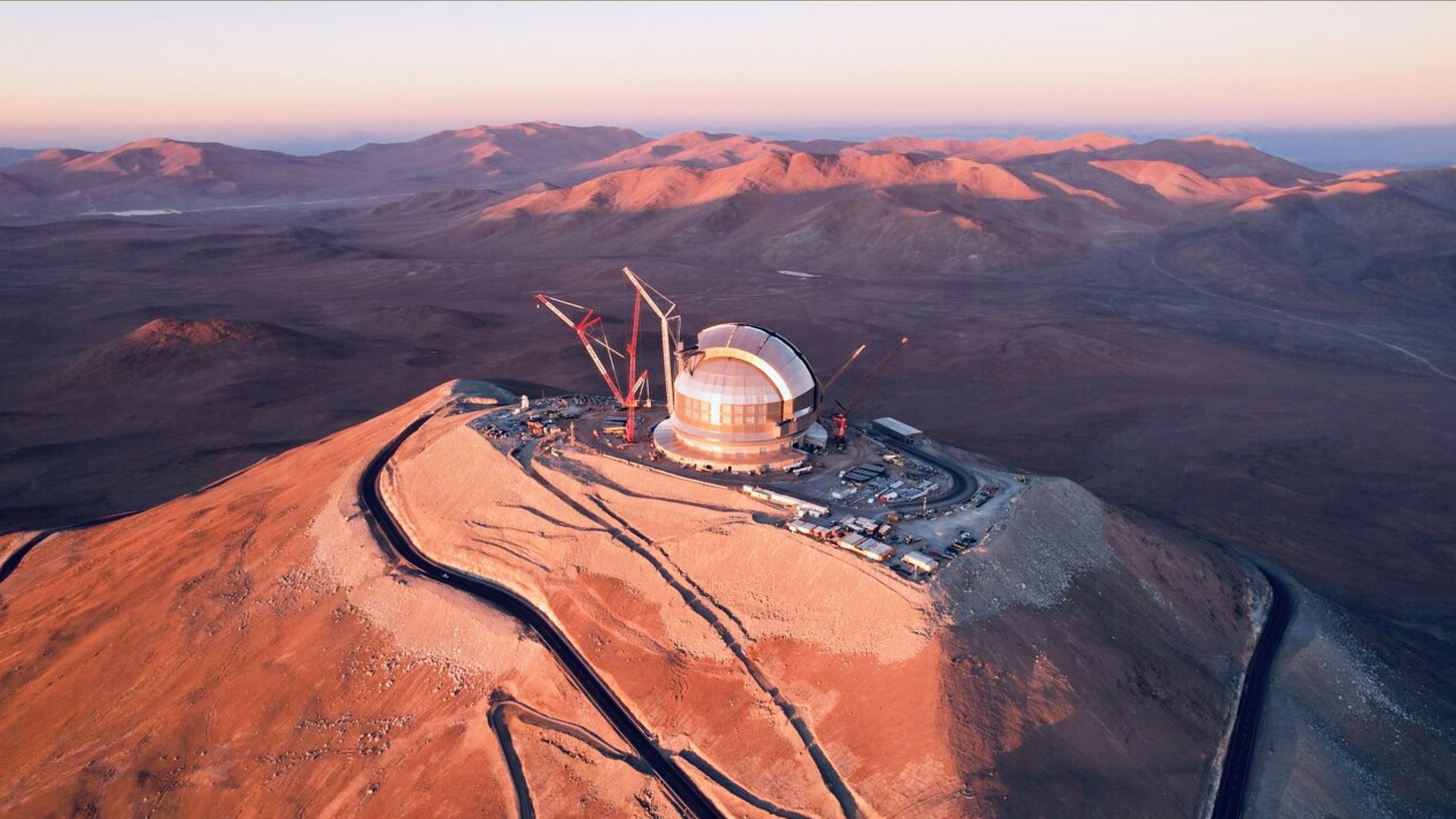 Aerial photograph of the Extremely Large Telescope under construction on Cerro Armazones in Chile's Atacama Desert at sunset.